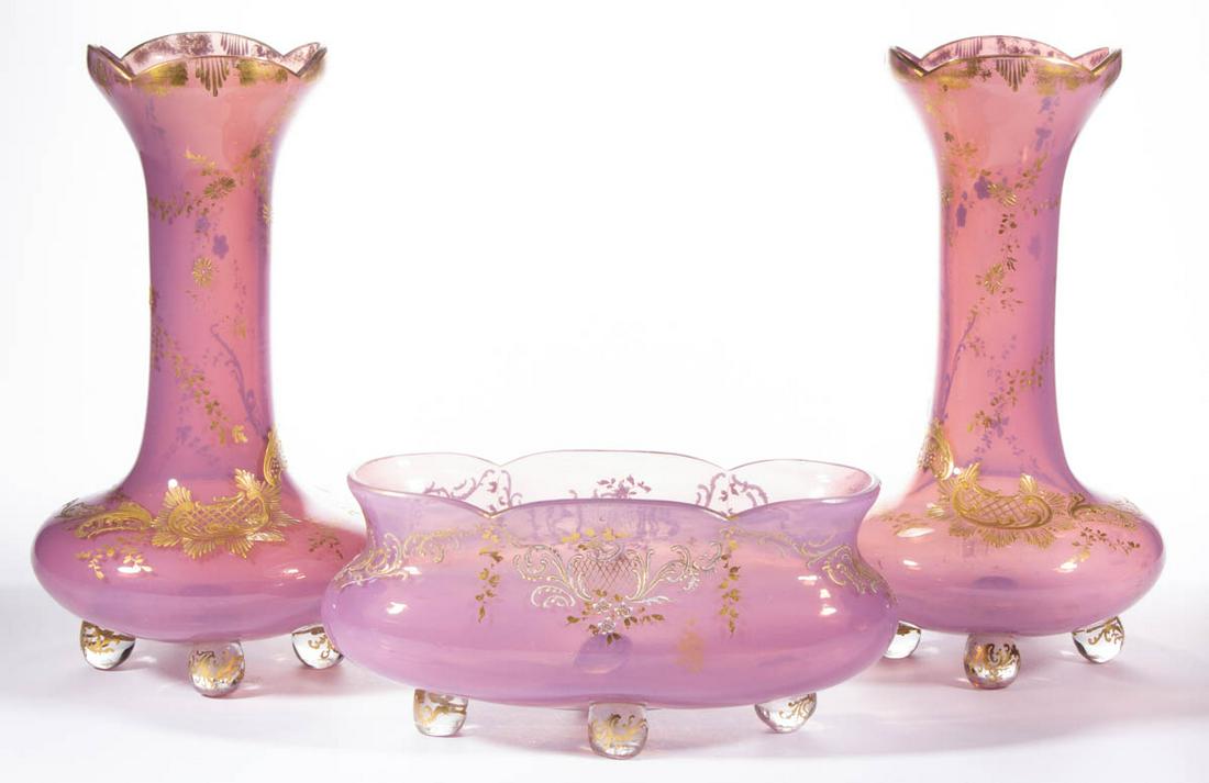 CONTINENTAL OPALINE GLASS THREE-PIECE CONSOLE SET: CONTINENTAL OPALINE GLASS THREE-PIECE CONSOLE SET, translucent purple/pink with gilt decoration, comprising a pair of matching bud vases with four applied colorless feet, and an ovoid centerpiece bowl