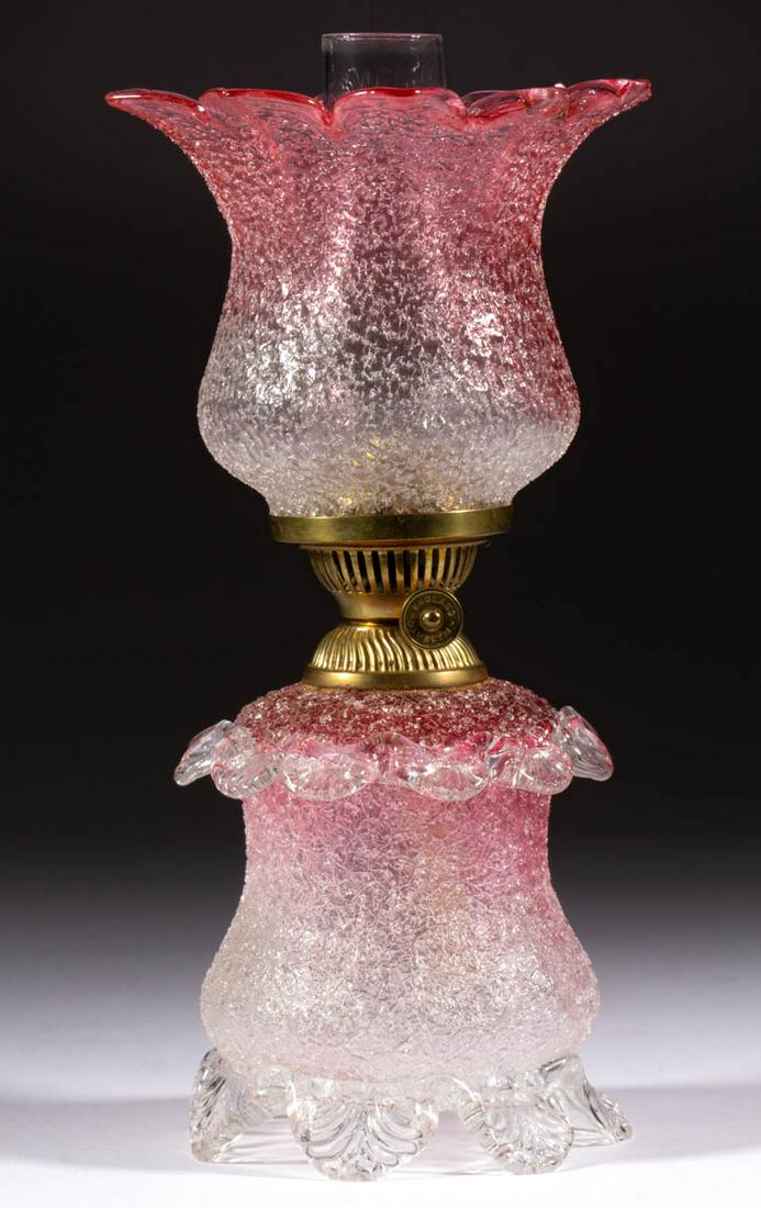OVERSHOT ART GLASS MINIATURE LAMP: OVERSHOT ART GLASS MINIATURE LAMP, rubina with colorless frit, cylinder-form font with concave medial, colorless applied base raised on seven toes, each with a pressed feather pattern, top with colorl