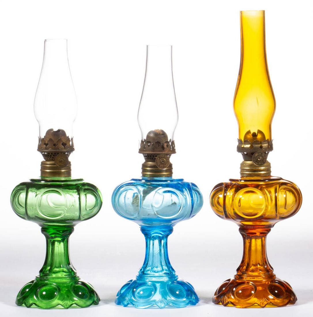 DAISY MINIATURE STAND LAMPS, LOT OF THREE: DAISY MINIATURE STAND LAMPS, LOT OF THREE, deep honey amber, blue and emerald green, period collars. Fitted with period Acorn burners, one amber and two colorless chimneys. First quarter 20th century.