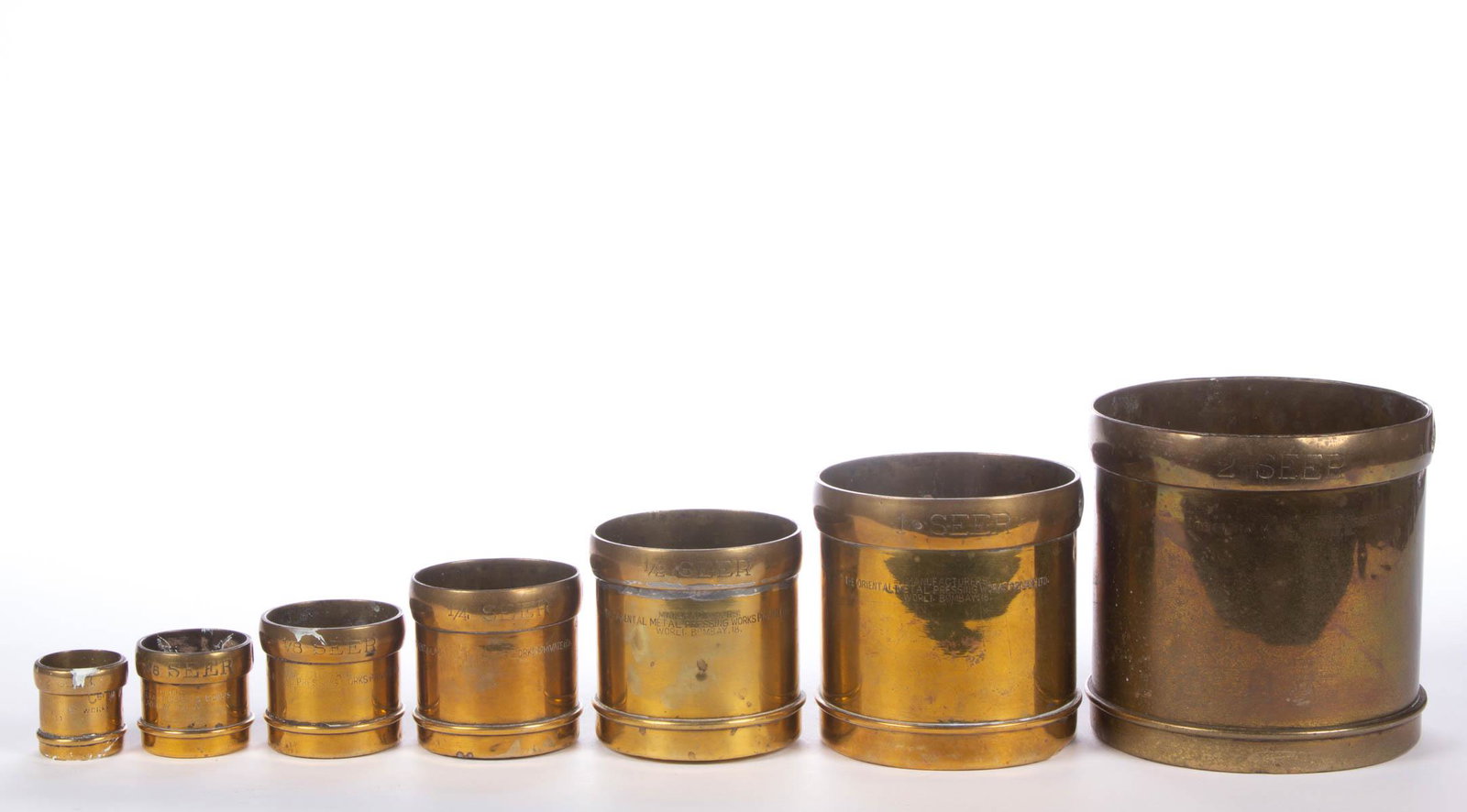 GRADUATED SET OF SEVEN BRITISH COLONIAL BRASS SEER: GRADUATED SET OF SEVEN BRITISH COLONIAL BRASS SEER MEASURES, each of cylindrical form marked "MANUFACTURERS, / ORIENTAL METAL PRESSING WORKS / WORLI. BOMBAY NO. 18". Late 19th/early 20th century. Larg