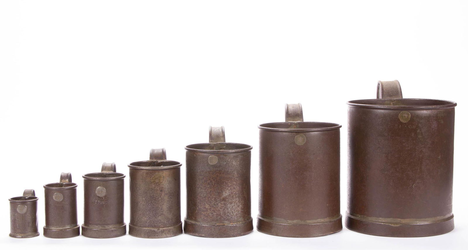 SET OF SEVEN BRITISH TIN MEASURES: SET OF SEVEN BRITISH TIN MEASURES, from "1/2 GILL" to "GALLON", each handled cylindrical form of seamed construction with rolled rim and applied foot, royal proof mark to body. Circa 1910. 2 3/4" to 9