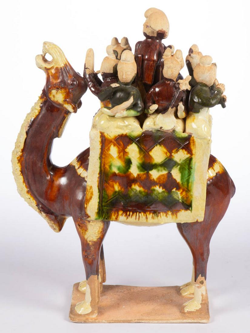 CHINESE TANG DYNASTY-STYLE CERAMIC FIGURAL GROUP: CHINESE TANG DYNASTY-STYLE CERAMIC FIGURAL GROUP, depicting eight figures, seven playing instruments, sitting on a standing camel fitted with a saddle and blanket. Unmarked. 20th century. 14 5/8" HOA.