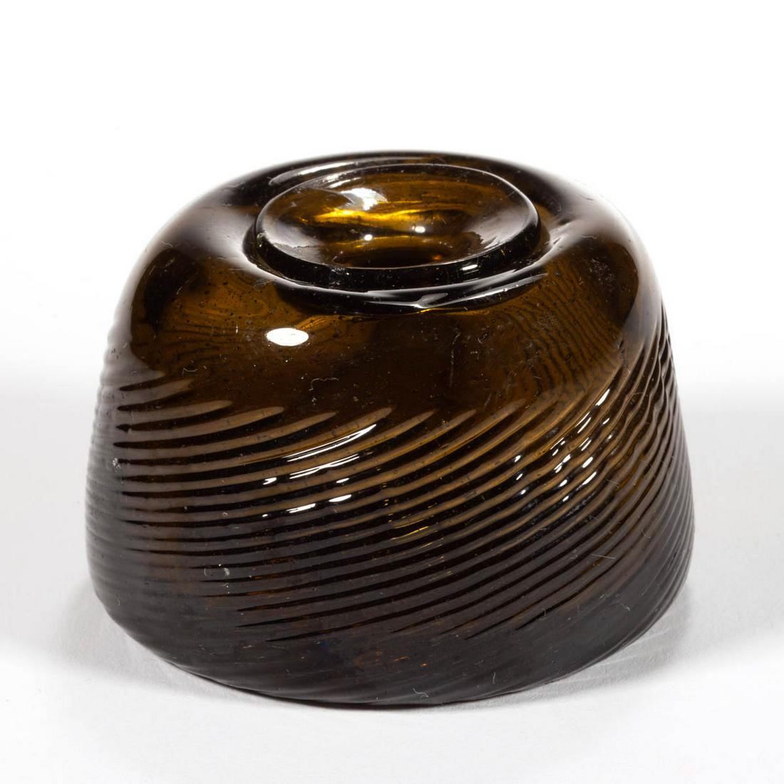 PATTERN-MOLDED PITKIN-TYPE INKWELL: PATTERN-MOLDED PITKIN-TYPE INKWELL, olive amber, conical form with ribs swirling to the right, slight kick-up base with a rough pontil mark. Probably New England. 1800-1830. 1 5/8" H, 2 1/4" D base. E