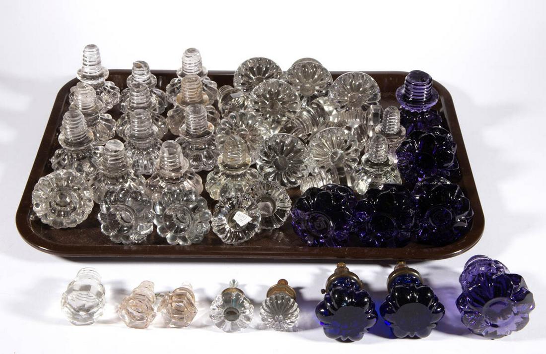 ASSORTED PRESSED GLASS FURNITURE KNOBS, LOT OF 46: ASSORTED PRESSED GLASS FURNITURE KNOBS, LOT OF 46, including six amethyst and two cobalt blue examples, remainder being colorless, eight having a period metal shank. Various makers. 19th century. 2" t