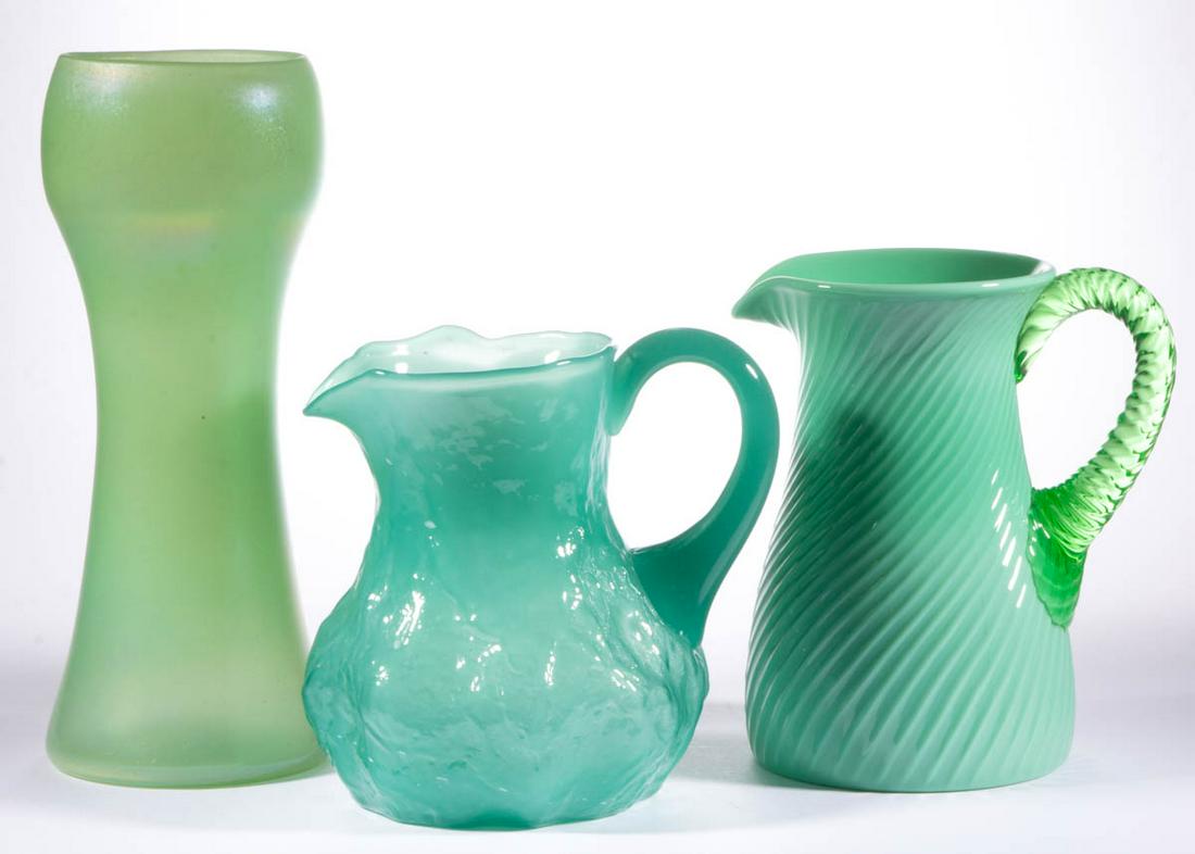 ASSORTED GREEN GLASS ARTICLES, LOT OF THREE: ASSORTED GREEN GLASS ARTICLES, LOT OF THREE, comprising a stretch glass vase, a translucent textured pitcher, and a opaque swirled pitcher with an applied green swirled handle. Various makers. 20th ce