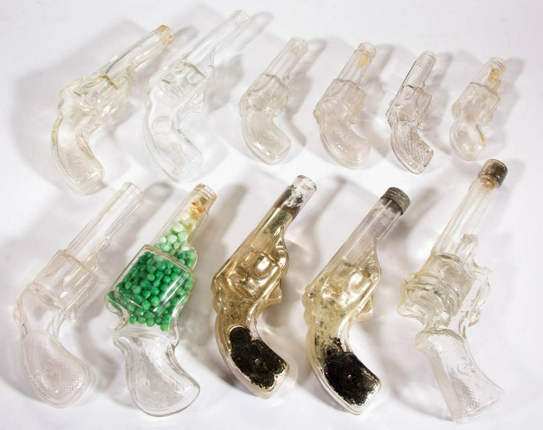 ASSORTED FIGURAL REVOLVER GLASS CANDY CONTAINERS, LOT: ASSORTED FIGURAL REVOLVER GLASS CANDY CONTAINERS, LOT OF 11, colorless, including two Black and Silver examples, a Medium Gun with Fancy Grip, and a Square Butt Revolver, one example having a lid, rem