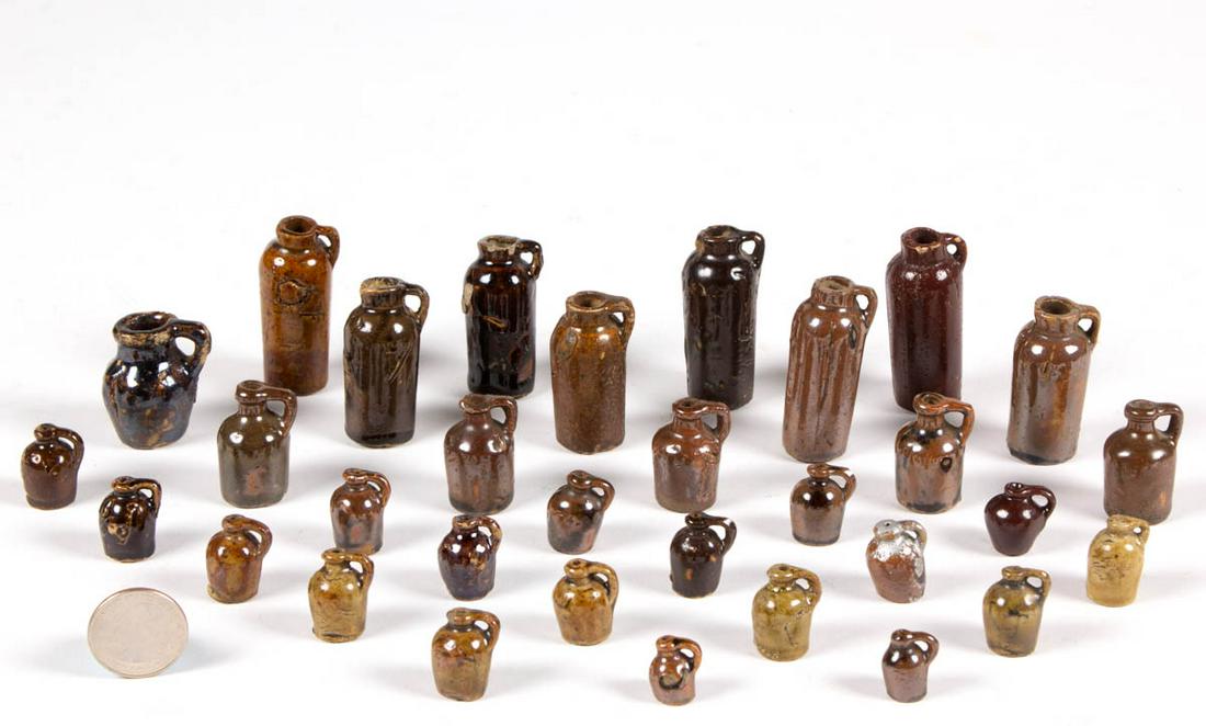 ASSORTED AMERICAN STONEWARE MINIATURE / DOLLHOUSE JUGS,: ASSORTED AMERICAN STONEWARE MINIATURE / DOLLHOUSE JUGS, LOT OF 32, Albany-slip, brown-, and Alkaline-glazed, each with handle, comprising 23 beehive form jugs, eight cylindrical bottles/jugs, and one 