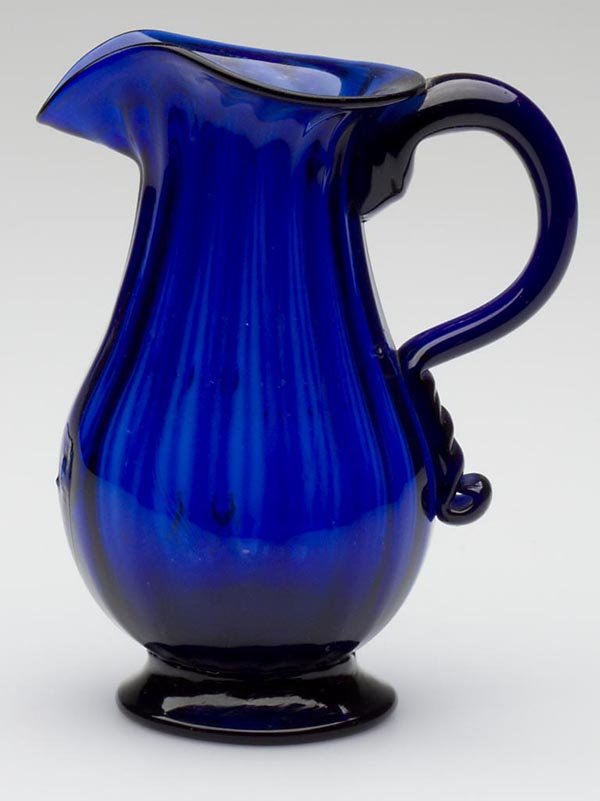 PATTERN-MOLDED CREAM PITCHER: PATTERN-MOLDED CREAM PITCHER, deep cobalt blue, pyriform body displaying 16 vertical ribs and an applied solid handle with an elongated terminal, raised on a solid flared foot with a rough pontil mark