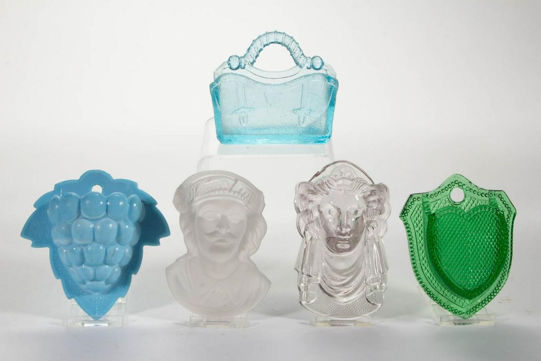 ASSORTED PRESSED NOVELTY GLASS HANGING MATCH HOLDERS,: ASSORTED PRESSED NOVELTY GLASS HANGING MATCH HOLDERS, LOT OF FIVE, comprising a colorless Jenny Lind, a blue Valise, an opaque blue Grapes, a green Heart, and a frosted colorless Columbus. Various mak