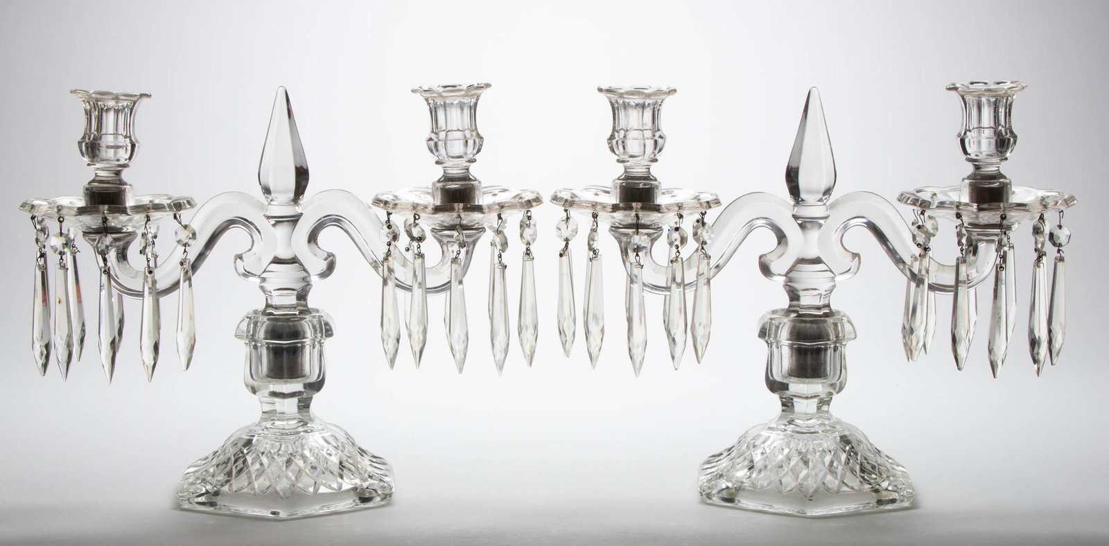 HEISEY PRESSED GLASS PAIR OF CANDELABRAS: HEISEY PRESSED GLASS PAIR OF CANDELABRAS, colorless, each having a two-arm form and being fitted into matching squat based with a diamond band to the foot, each having hanging prisms. A. H. Heisey & C