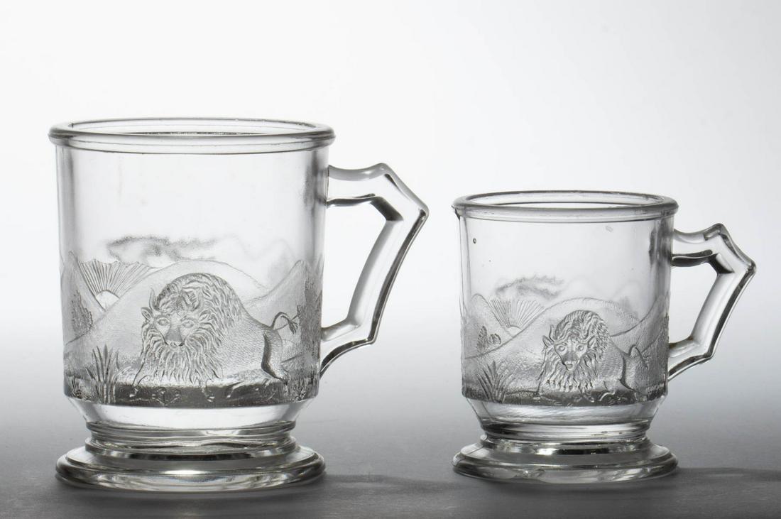 WESTWARD HO / PIONEER (OMN) MUGS, LOT OF TWO: WESTWARD HO / PIONEER (OMN) MUGS, LOT OF TWO, colorless, including a toy example. Gillinder & Sons, Philadelphia, PA. Circa 1879. 2 3/4" and 3 1/2" H.