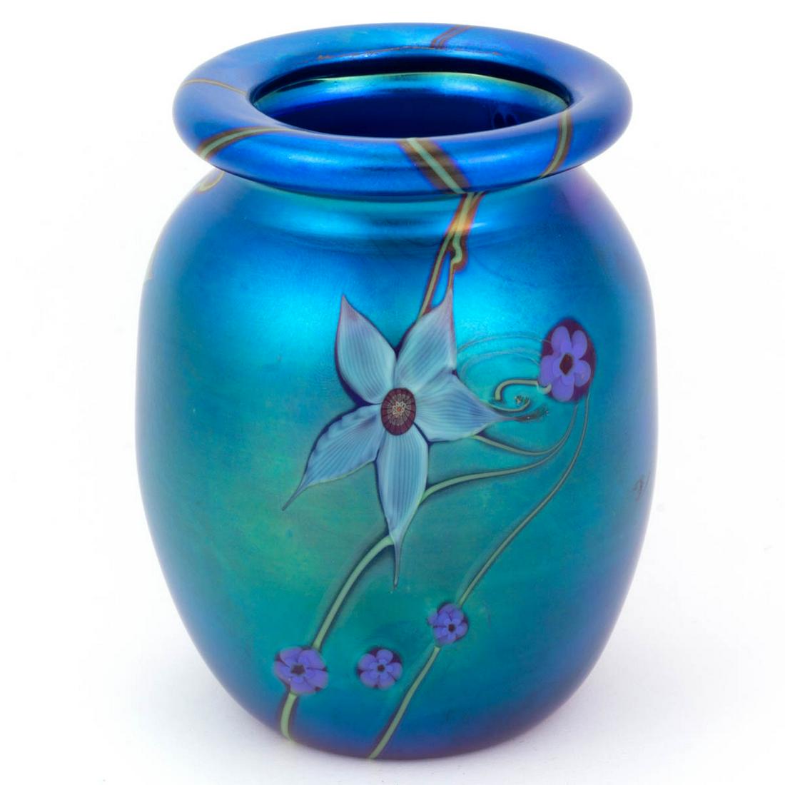 ORIENT & FLUME FLORAL VINE IRIDESCENT STUDIO ART GLASS: ORIENT & FLUME FLORAL VINE IRIDESCENT STUDIO ART GLASS VASE, blue ground, having three vertical thin green vines supporting a white flower and scattered blue millefiori blooms, folded-over rim, signed