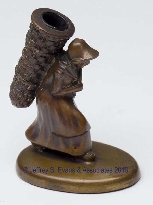 BRONZE FIGURAL THIMBLE HOLDER: BRONZE FIGURAL THIMBLE HOLDER, depicting a lady with basket on back. Late 19th/early 20th century. 4 1/8" h overall, 2 1/4" xx 3 1/4". Provenance: Collection of the late Fern I. Hill.