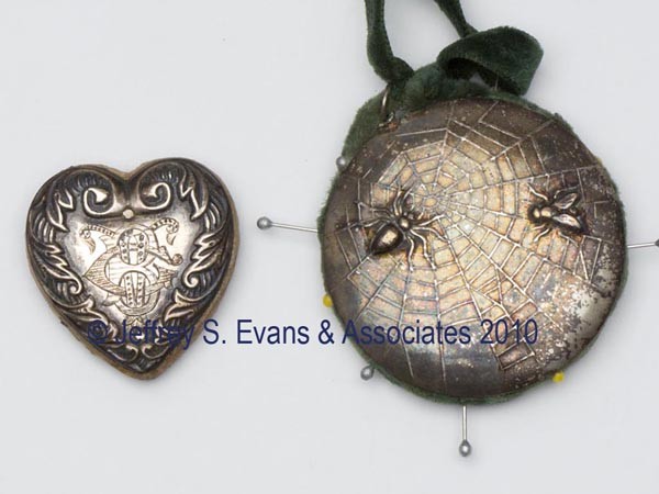 SILVER-LIKE FIGURAL PIN CUSHIONS, LOT OF TWO: SILVER-LIKE FIGURAL PIN CUSHIONS, LOT OF TWO, consisting of a heart form with scroll pattern and monogram; and a spider web with spider and fly, green velvet cushion with matching ribbon. Late 19th/ea