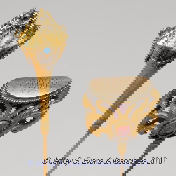 TWO GOLD-TONE HATPINS: TWO GOLD-TONE HATPINS, comprised of a reticulated Art Nouveau top set with two pink stones and a monogrammed crown, and a peaked conical top with applied bow-knot wreaths and tiny turquoise-like stone