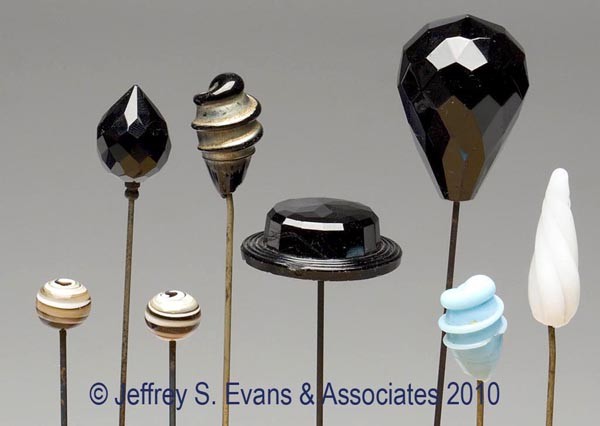 EIGHT ASSORTED GLASS HATPINS: EIGHT ASSORTED GLASS HATPINS, including opaque black, blue, white, and swirled examples, gold-colored and steel pins. First quarter 20th century. 8 1/2" to 11 1/2" long. Provenance: Hilda Fried estate