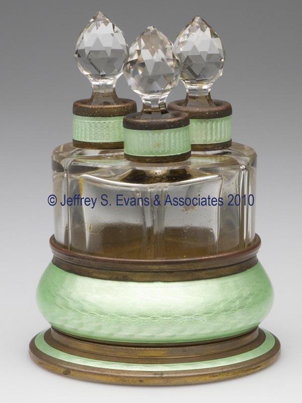 AUSTRIAN ENAMEL ON GILT-BRASS MOUNTED COLOGNE SET: AUSTRIAN ENAMEL ON GILT-BRASS MOUNTED COLOGNE SET, comprised of three triangular-shape colorless glass bottles in a fitted base, original facet-cut stoppers, base marked "I. CNK" and Made in Austria u