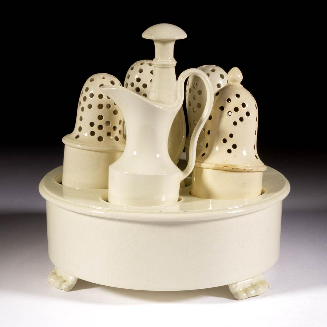 ENGLISH WEDGWOOD CREAMWARE SIX-PIECE ASSEMBLED CRUET /: ENGLISH WEDGWOOD CREAMWARE SIX-PIECE ASSEMBLED CRUET / CONDIMENT SET, comprising a tri-footed circular stand with central handle and five circular holders, four pepper pots including one with finial,