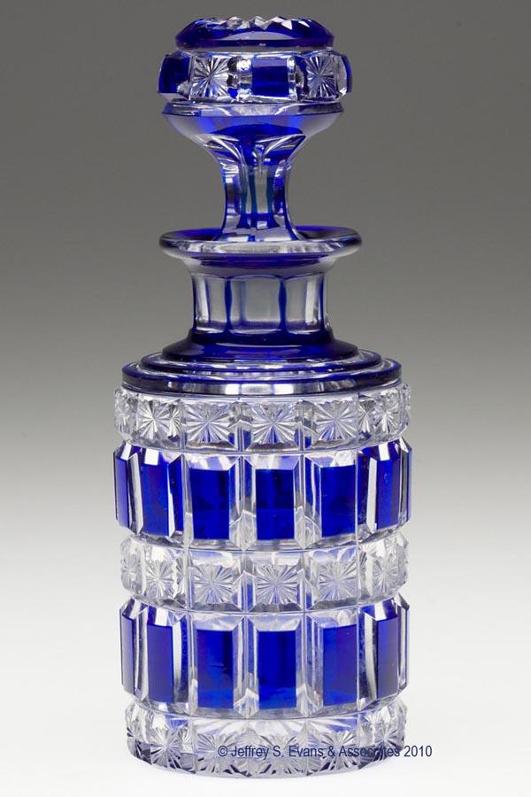 CUT OVERLAY PANEL AND STAR COLOGNE BOTTLE: CUT OVERLAY PANEL AND STAR COLOGNE BOTTLE, deep cobalt blue to colorless, cylindrical form with a stepped shoulder, short panel-cut neck, flanged mouth, and star-cut base, original air-trap stopper wi