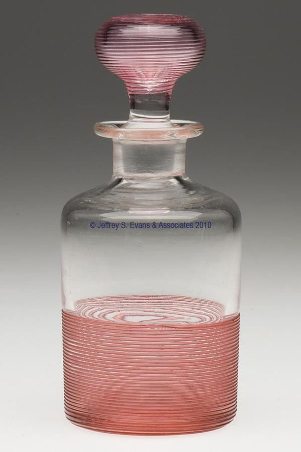 BLOWN AND THREADED COLOGNE BOTTLE: BLOWN AND THREADED COLOGNE BOTTLE, colorless with rose-color threads, cylindrical form with a short neck and flanged mouth, threading from medial body continuing under base to the polished pontil mark
