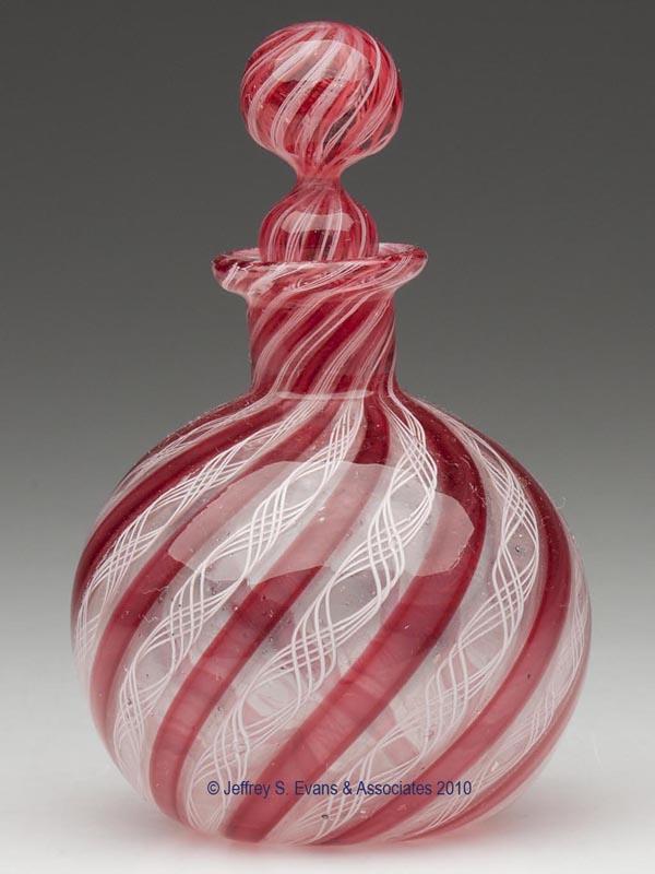 BLOWN LATTICINIO STYLE COLOGNE BOTTLE: BLOWN LATTICINIO STYLE COLOGNE BOTTLE, colorless with red stripes alternating with opaque white twists, globular form with a short neck and rough pontil mark, original marble-style stopper. United Sta