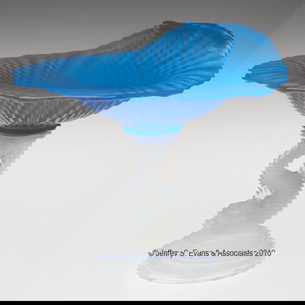 PRESSED SHELL AND DOLPHIN COMPOTE: PRESSED SHELL AND DOLPHIN COMPOTE, translucent starch blue and fiery opalescent, the shallow bowl with one turned-up side, raised on a small dolphin standard and stepped circular foot with a rough pon