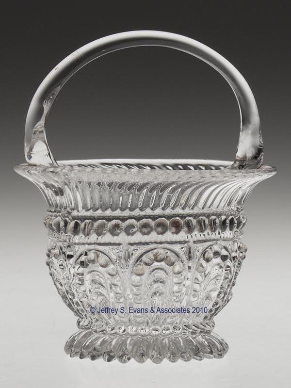 BLOWN-MOLDED GV-24 BASKET SALT: BLOWN-MOLDED GV-24 BASKET SALT, colorless, flared rim with an applied handle, raised on a slight foot with narrow lobes and a rough pontil mark. Probably Europe. Second half 19th century. 4" HOA, 2 3/