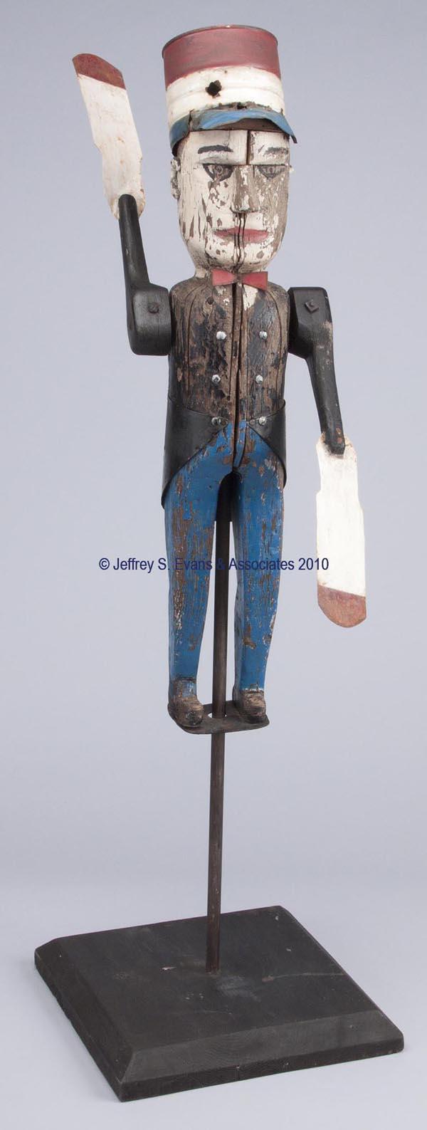AMERICAN CARVED AND PAINTED WOOD WHIRLIGIG: AMERICAN CARVED AND PAINTED WOOD WHIRLIGIG depicting a stationmaster, painted sheet-iron bow-tie, tails, hat, and arm paddles. On a contemporary display mount. First half 20th century. 24 1/2" H. Prov