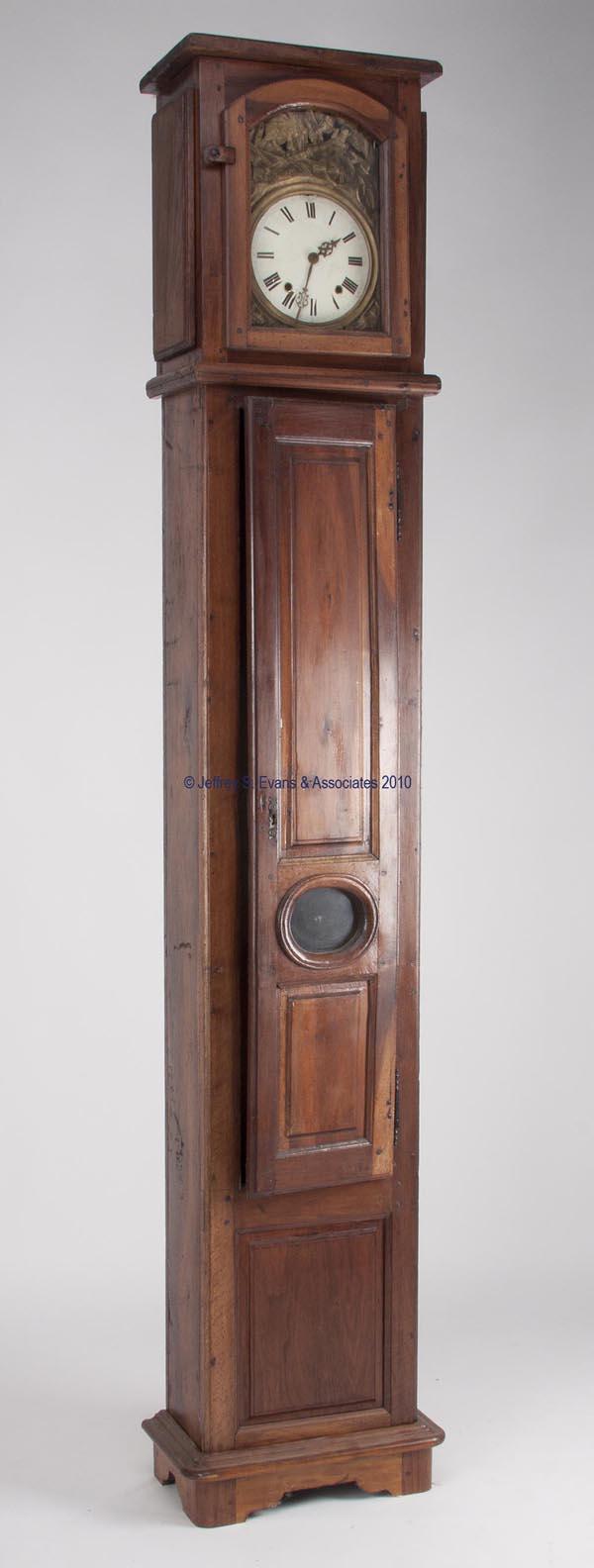 FRENCH PROVINCIAL WALNUT AND OAK LONG CASE CLOCK: FRENCH PROVINCIAL WALNUT AND OAK LONG CASE CLOCK Morbier style with enamel face and gilt-brass surround, multi-section case with raised front panels, folding pendulum and two iron weights. 19th centur