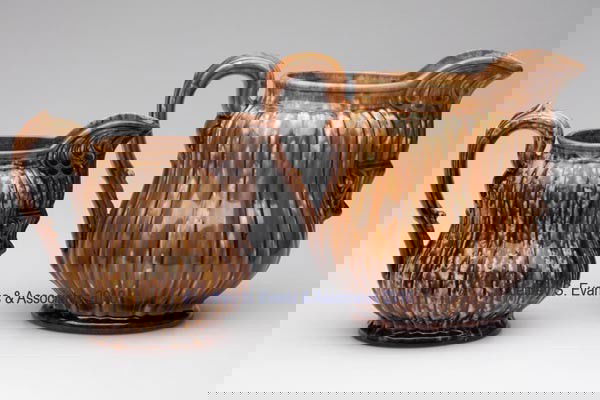 BENNINGTON FLINT ENAMEL AND ROCKINGHAM-GLAZE POTTE: BENNINGTON FLINT ENAMEL AND ROCKINGHAM-GLAZE POTTERY PITCHERS, LOT OF TWO mottled brown glaze, large example flint enamel with orange and green, each Alternate Rib pattern with impressed Type A mark,