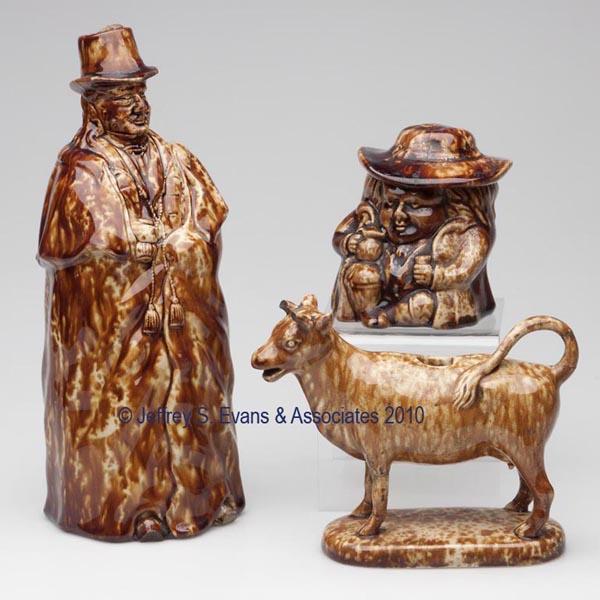 BENNINGTON ROCKINGHAM-GLAZE POTTERY FIGURAL ARTICL: BENNINGTON ROCKINGHAM-GLAZE POTTERY FIGURAL ARTICLES, LOT OF THREE mottled brown glaze, comprising a Coachman bottle with impressed Type A mark, a Toby snuff jar, and a cow creamer lacking lid. Lyman