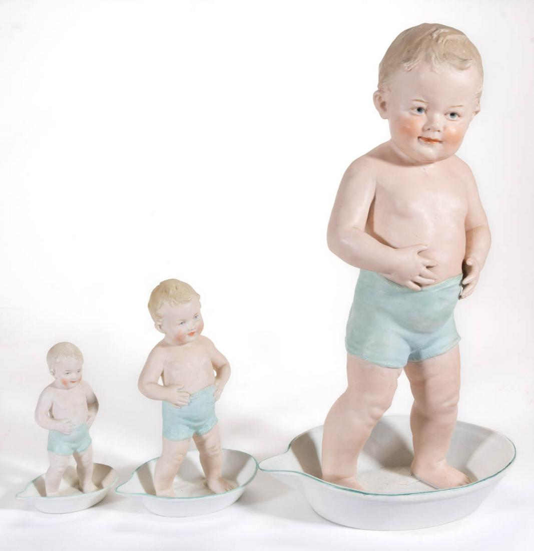 GERMAN GEBRUDER HEUBACH BISQUE PORCELAIN FIGURES, LOT: GERMAN GEBRUDER HEUBACH BISQUE PORCELAIN FIGURES, LOT OF THREE, each having polychrome hand-painted decorations featuring a boy wearing light blue shorts and standing in an oval wash pan with spout to