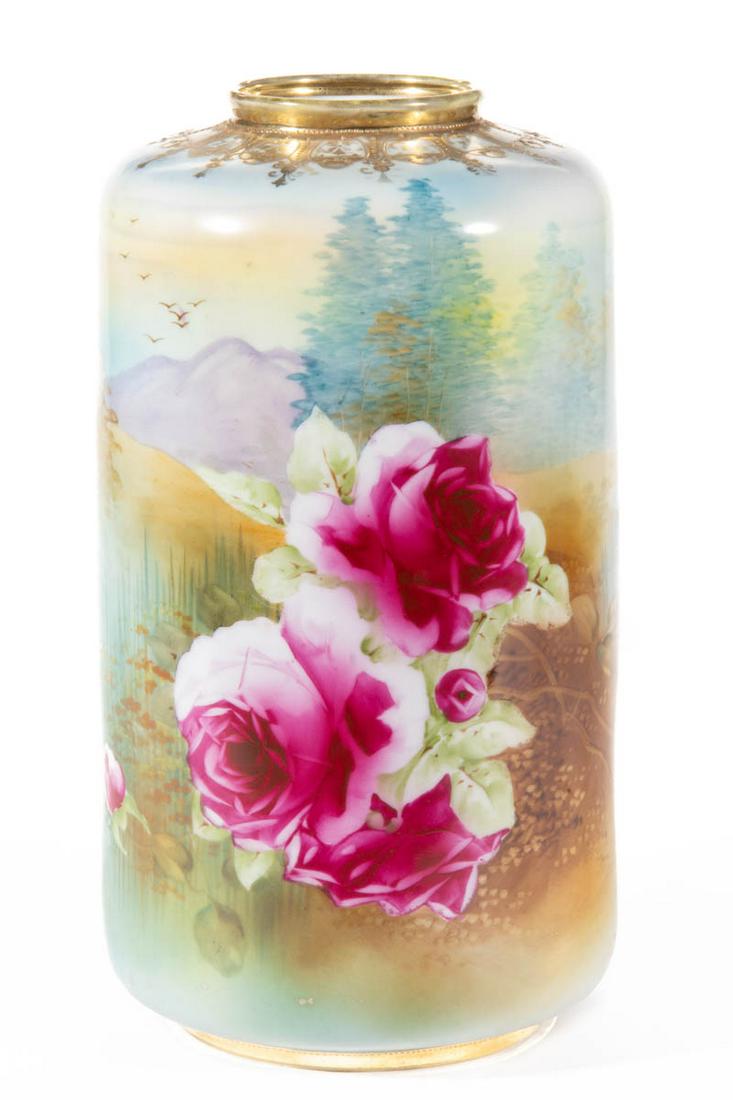 JAPANESE NIPPON HAND-PAINTED PORCELAIN VASE: JAPANESE NIPPON HAND-PAINTED PORCELAIN VASE, cylindrical form, featuring polychrome landscape with bold pink roses in foreground and serene water and mountain background scene, having raised gilt deco