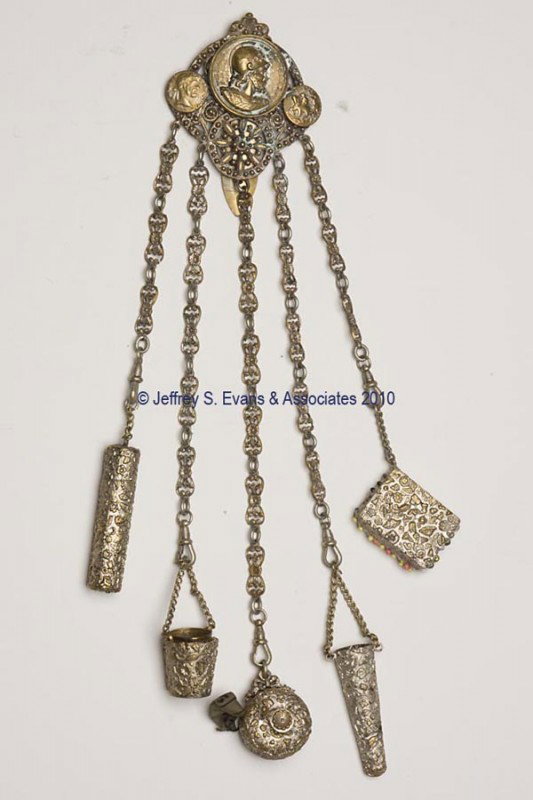 GILT-METAL FIGURAL NEEDLEWORKING CHATELAINE: GILT-METAL FIGURAL NEEDLEWORKING CHATELAINE, hinged clip attached to a plaque embossed with a Roman soldier and two coin-like discs on a beaded medallion, suspending five floral chains and matching he