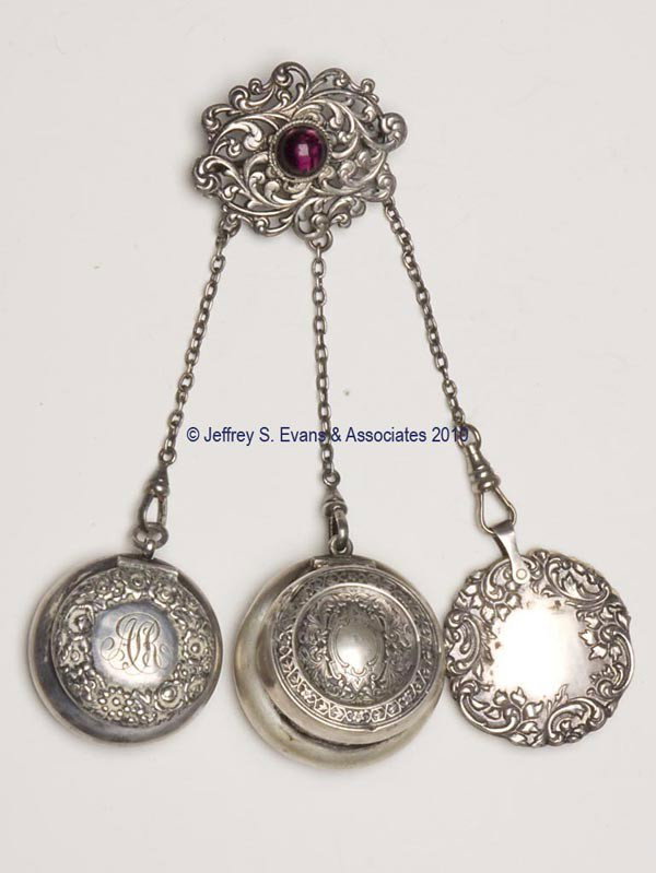 SILVER-LIKE DANCE CHATELAINE: SILVER-LIKE DANCE CHATELAINE, brooch pin attached to an entwined scroll pattern plaque with an amethyst color stone, suspending three chains and three non-matching patterned sterling silver appendages