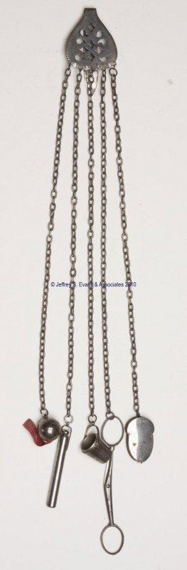 STEEL NEEDLEWORKING CHATELAINE: STEEL NEEDLEWORKING CHATELAINE, solid clip and plaque with stylized cut-outs, suspending five chains and five appendages. Appendages consist an acorn-form pin cushion; folding scissors; a needle case;