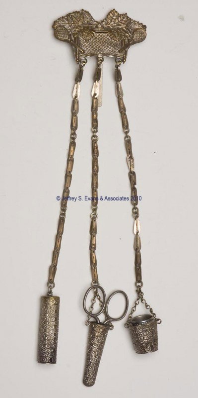FIGURAL GILT-METAL NEEDLEWORKING CHATELAINE: FIGURAL GILT-METAL NEEDLEWORKING CHATELAINE, hinged clip attached to a plaque with a wreath over a net and two tennis rackets, suspending three chains and three matching floral-patterned appendages co