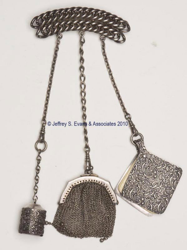 SILVER-PLATED DANCE CHATELAINE: SILVER-PLATED DANCE CHATELAINE, brooch pin attached to a rope pattern plaque suspending three chains and three non-matching patterned appendages consisting of a coin dispenser, memo book, and a marked