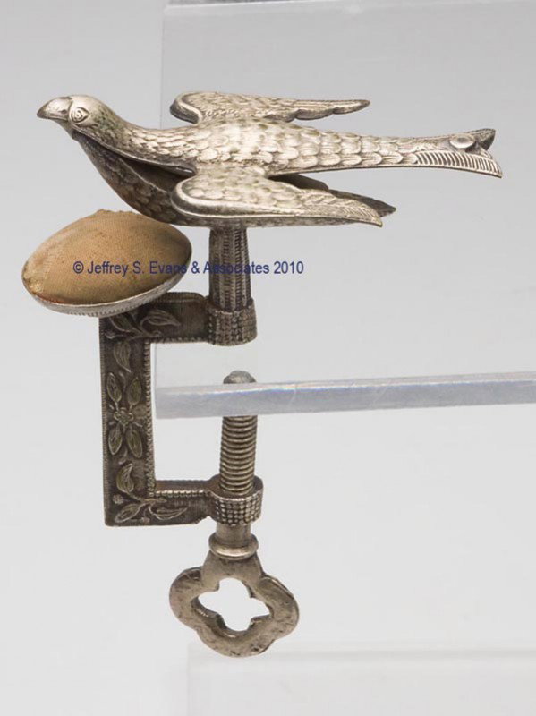 SILVER-PLATED BRASS SEWING BIRD CLAMP WITH PIN CUSH: SILVER-PLATED BRASS SEWING BIRD CLAMP WITH PIN CUSHION, molded and cast ornamentation, original tan velvet covered pin cushion under bird. Second half 19th century. 4 3/8" h overall. Provenance: Colle