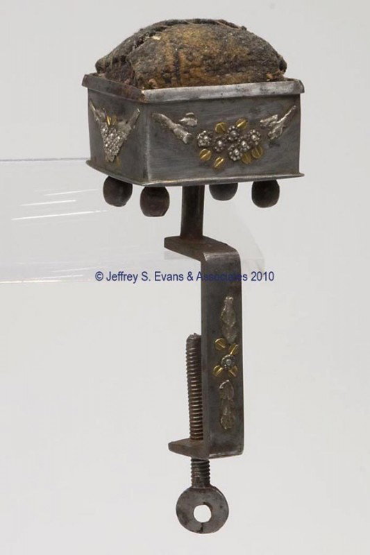 STEEL WITH TULA WORK SEWING CLAMP WITH PIN CUSHION: STEEL WITH TULA WORK SEWING CLAMP WITH PIN CUSHION, rectangular form with four bun feet, applied gilded metal floral and foliage embellishments, attached to a c-clamp with matching decoration, fabric 