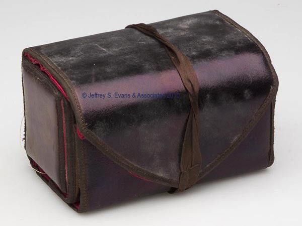 LEATHER ROLL-OUT SEWING WORK CASE: LEATHER ROLL-OUT SEWING WORK CASE, black with brown silk trim and a ribbon for closure, opens to a red silk lined interior, fitted with a large sleeve, four sleeves for needle packets, three wool leav
