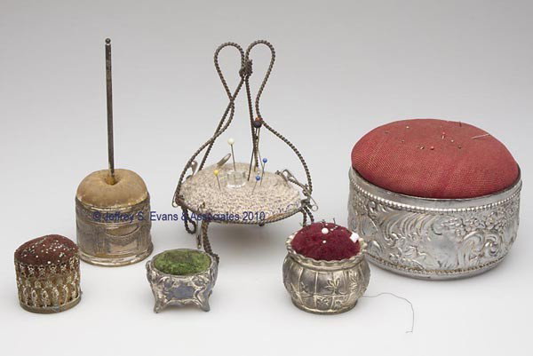 SILVER-PLATED PIN CUSHIONS, LOT OF FIVE: SILVER-PLATED PIN CUSHIONS, LOT OF FIVE, consisting of a scroll and floral embossed example with lift-off pin cushion, interior fitted with a red silk lined compartment; a footed example; and three ot