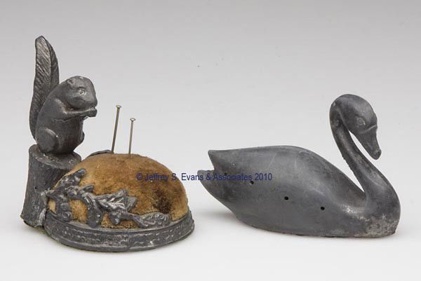 VARIOUS METALS FIGURAL PIN CUSHIONS, LOT OF TWO: VARIOUS METALS FIGURAL PIN CUSHIONS, LOT OF TWO, consisting of a silver-plated swan and a spelter squirrel sitting on a stump eating a nut. First quarter 20th century. Swan 2 1/8" h and squirrel 2 3/4