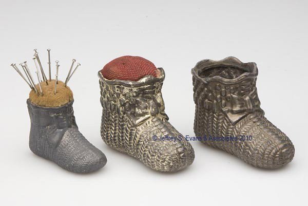VARIOUS METALS FIGURAL PIN CUSHIONS, LOT OF THREE: VARIOUS METALS FIGURAL PIN CUSHIONS, LOT OF THREE, each depicting a baby bootie, two with original pin cushions. Late 19th/early 20th century. Various sizes. Provenance: Collection of the late Hilda F