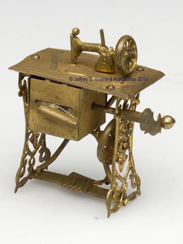 FRIEDLAND BRASS FIGURAL TAPE MEASURER: FRIEDLAND BRASS FIGURAL TAPE MEASURER, depicting a treadle sewing machine, table stamped "Friedland", wind-up handle, cotton tape calibrated in centimeters. Late 19th/early 20th century. 2 1/4" h over