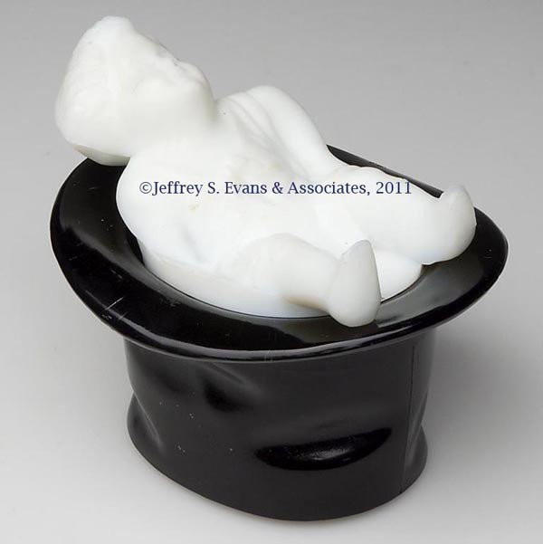 BABY IN TOP HAT MATCH HOLDER: BABY IN TOP HAT MATCH HOLDER, baby is opaque white with satin finish, top hat is opaque black glossy finish, underside of cover is a match striker. Late 19th/early 20th century. 4 1/4" H, 4" x 4 3/4".