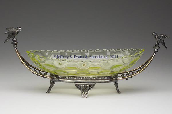 INVERTED THUMBPRINT AND HEART OPTIC CELERY TRAY: INVERTED THUMBPRINT AND HEART OPTIC CELERY TRAY, vaseline, fitted in a Pairpoint quadruple plate stand, with a bird at each end. Fourth quarter 19th century. 6 1/4" HOA, 3" x 15 1/2". Provenance: Coll