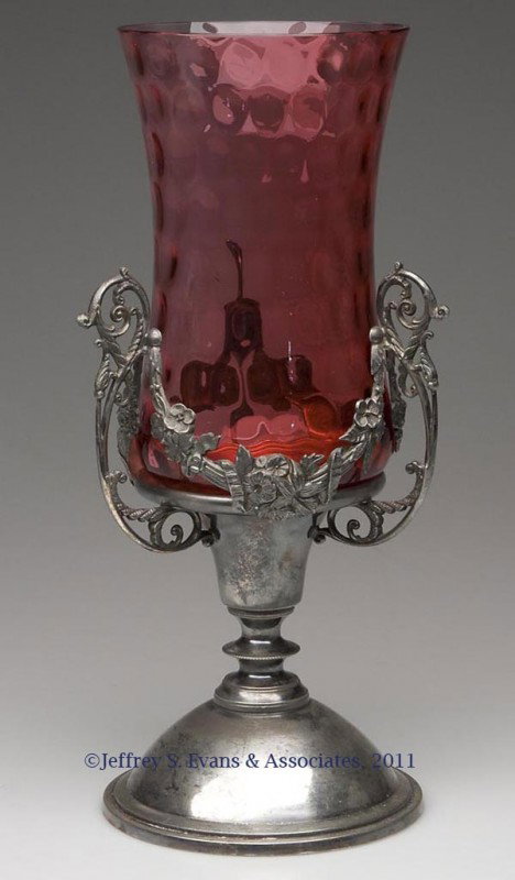 CRANBERRY INVERTED THUMBPRINT CELERY VASE IN PAIRP: CRANBERRY INVERTED THUMBPRINT CELERY VASE IN PAIRPOINT STAND, pedestalled base with three handles and floral swag decoration, base marked "PAIRPOINT MFG. CO. NEW BEDFORD MASS. / QUADRUPLE PLATE" and "