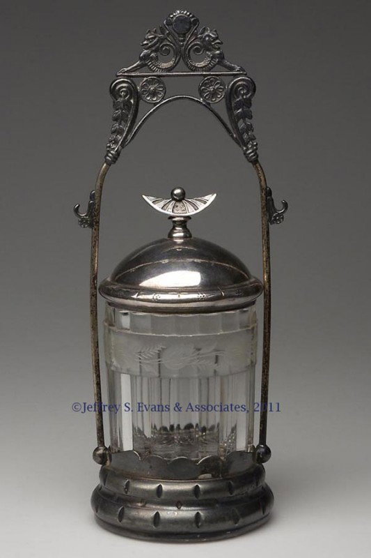 VICTORIAN PICKLE CASTER: VICTORIAN PICKLE CASTER, colorless pressed-glass jar with engraved floral decoration, fitted in a Pairpoint quadruple-plate stand, lacking tongs and fork. Fourth quarter 19th century. 11 1/2" HOA, jar