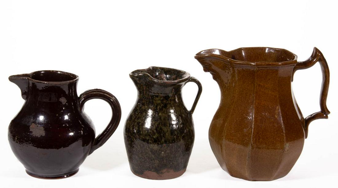 ASSORTED AMERICAN POTTERY JUGS / PITCHERS, LOT OF THREE: ASSORTED AMERICAN POTTERY JUGS / PITCHERS, LOT OF THREE, comprising a ten-sided brown-glazed example with molded mask spout, a redware lead-glazed example with triple-ridged handle, and an approximate